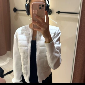 Vit vår jacka - Säljer en stilren vit bomberjacka med dragkedja. Jackan har en quiltad design och långa ärmar, perfekt för en trendig look. Det är som en cardigan oxå