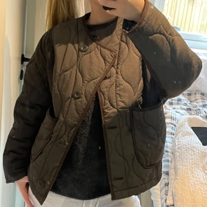 Olivgrön quiltad jacka från Zara - Säljer en olivgrön quiltad jacka från Zara med knappar framtill. Jackan har en rund halsringning och stora fickor på sidorna. Resår i ryggen. Passar XS/S beroende på hur du vill att den ska sitta!