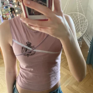 Rosa ärmlös topp med tryck - Säljer en rosa ärmlös topp med ett unikt tryck framtill och dekorativa band över bröstet. Perfekt för en trendig och avslappnad stil. Passar bra till jeans eller kjol.
