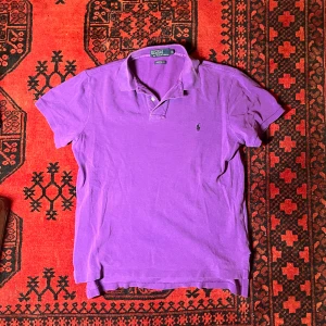 Lila pikétröja från Ralph Lauren - Säljer en snygg lila pikétröja från Ralph Lauren. Tröjan har en klassisk krage och korta ärmar med en liten broderad logga på bröstet. Perfekt för en stilren look!