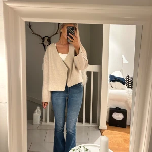 Beige omlott cardigan - Säljer en stilren beige omlott cardigan med långärmad design. Perfekt för en avslappnad look. Den har en lös passform och är tillverkad i ett mjukt material.