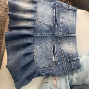 Blå jeanskjol med volang - Snygg blå jeanskjol med volangdetaljer och fickor både fram och bak. Kjolen har en klassisk jeansknapp och bälteshällor för extra stil. Perfekt för en avslappnad look.