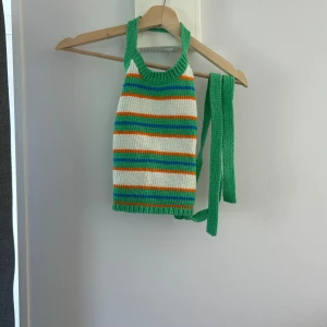 Randig stickad topp från Zara - Säljer en färgglad randig stickad topp från Zara i grönt, vitt, orange och blått. Toppen har en halterneck-design med knytband och är ärmlös. Perfekt för sommarn 