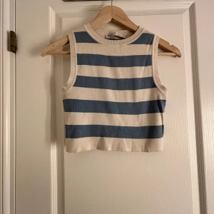 Randig ärmlös topp från Zara - Säljer en snygg ärmlös topp från Zara med breda blå och vita ränder. Perfekt för sommardagar eller som ett lager under en jacka. Toppen har en ribbad kant vid halsen och ärmarna.