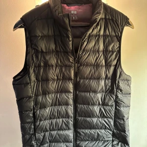 Svart dunväst med dragkedja - Snygg och praktisk svart dunväst med dragkedja. Perfekt för kyligare dagar och lätt att matcha med olika outfits. Västen har en stilren design och är idealisk för lager-på-lager-stil.