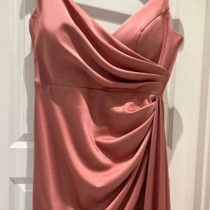 Rosa axelbandslös klänning - Elegant rosa axelbandslös klänning med draperad design och omlott-detalj. Perfekt för festliga tillfällen med sin långa längd och mjuka material.