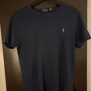 Mörkblå t-shirt från Ralph Lauren - Säljer en stilren mörkblå t-shirt från Ralph Lauren med en liten broderad logga på bröstet. T-shirten har en normal passform och är kortärmad, perfekt för en avslappnad look.