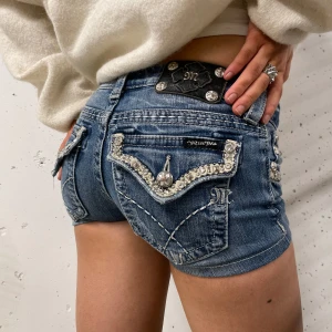 Jeansshorts från missme - Snygga jeansshorts från Miss Me med coola pärldetaljer på fickorna och en unik broderad design. De har en lågmidjad passform😊
