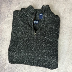 Grå stickad tröja från Chaps - Säljer en snygg grå stickad tröja från Chaps med dragkedja vid halsen. Perfekt för kyligare dagar med sin mjuka och bekväma passform. Tröjan har en melerad look som ger den en modern touch.