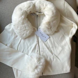 Vit jacka med fuskpälsdetaljer från NA-KD  - Elegant vit jacka från NAKD med mjuk fuskpäls på krage och ärmslut. Jackan har knappar framtill och en stilren design som passar perfekt för kyligare dagar. Pälsen är avtagbar.