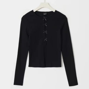 Svart ribbad topp med rosetter - Snygg svart ribbad topp med långa ärmar och dekorativa rosetter framtill. Perfekt för en stilren look.