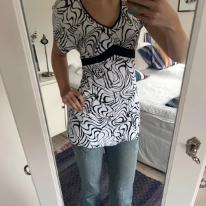 Svartvit mönstrad klänning med knytband - Säljer en svartvit klänning med abstrakt mönster och v-ringning. Den har korta ärmar och ett svart knytband i midjan som ger en fin siluett. Skriv vid frågor!🩷