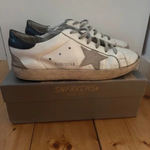 Vita sneakers med stjärndetalj - Snygga vita sneakers från Golden Goose med en grå stjärna på sidan och svarta detaljer vid hälen. Skorna har en vintage-look med snörning och en bekväm passform. Perfekta för en avslappnad stil.
