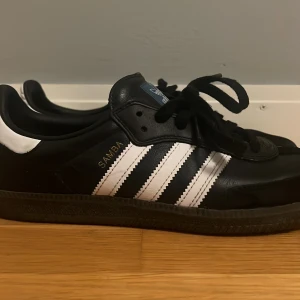 Adidas Samba i svart och vitt i storlek 43 men passar 42 och 44 - Klassiska Adidas Samba sneakers i svart och vitt. Skorna har de ikoniska tre ränderna på sidan och är tillverkade i skinn. Perfekta för en stilren och sportig look. Storlek 43 men passar även 42 
