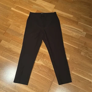 Svarta byxor från Gina Tricot - Snygga svarta byxor från Gina Tricot i storlek 38. De har en klassisk design med knapp och dragkedja framtill. Perfekta för en stilren look.