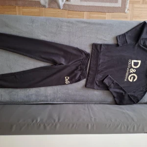 Svart hoodie från Dolce & Gabbana - Säljer en svart hoodie från Dolce & Gabbana med stort D&G-tryck i guld på framsidan. Tröjan har långa ärmar och en klassisk huva. Perfekt för en stilren och bekväm look.