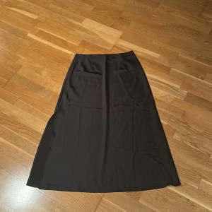 Svart långkjol från BikBok - Elegant svart långkjol från BikBok i storlek M. Kjolen har en stilren design med en diskret slits på sidan som ger en snygg detalj. Perfekt för en chic och minimalistisk look.