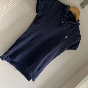 Mörkblå pikétröja från Ralph Lauren - Säljer en stilren mörkblå pikétröja från Ralph Lauren. Tröjan har en klassisk krage med knappar och det ikoniska broderade logotypen på bröstet. Perfekt för en avslappnad men ändå snygg look. Priset börjar vid 300kr men kan diskuterad med snabb affär!