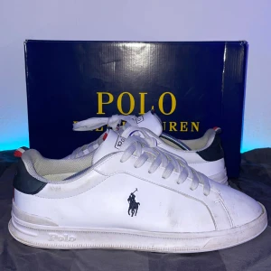 Ralph Lauren - Snygga vita sneakers från Polo Ralph Lauren med klassisk logga på sidan. Skorna har snörning och en stilren design med mörkblå och röda detaljer på hälen. Perfekta för en casual look. Box följer med🥳🙌🏼