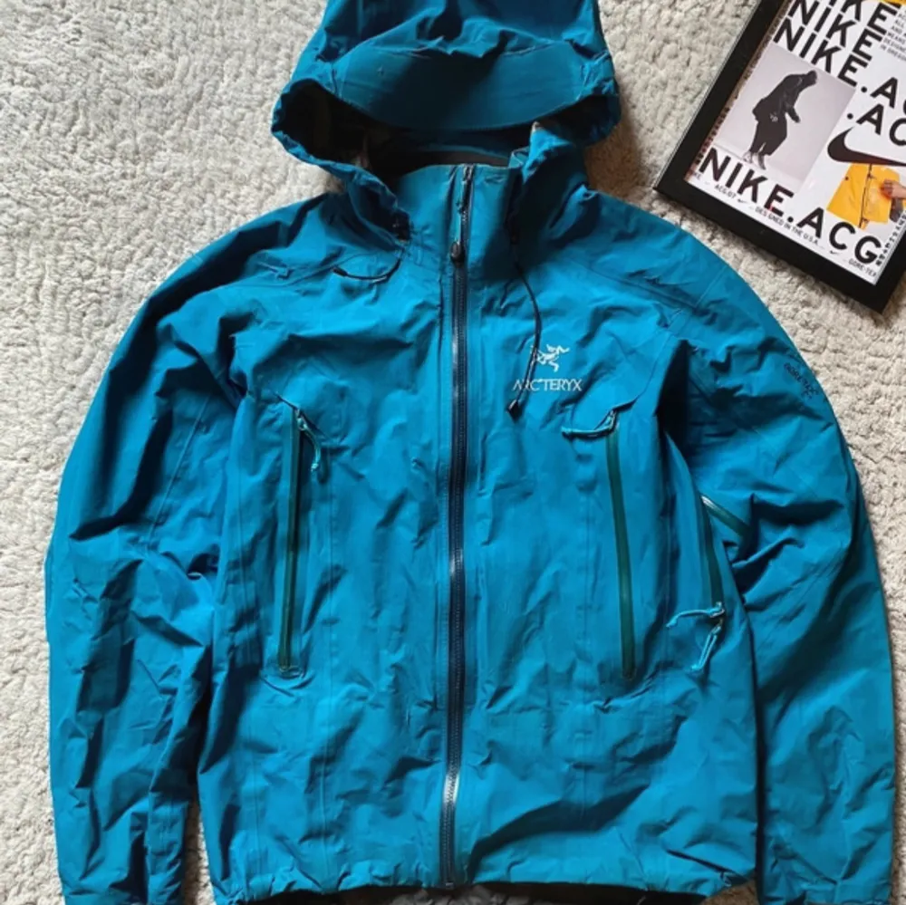 Säljer en blå vindjacka från Arc'teryx med huva och dragkedja. Jackan är tillverkad i Gore-Tex-material och har praktiska fickor med dragkedjor. Perfekt för utomhusaktiviteter och skyddar mot väder och vind. Pris går att diskutera, För fler bilder eller frågor så skriv till mig! . Takit.