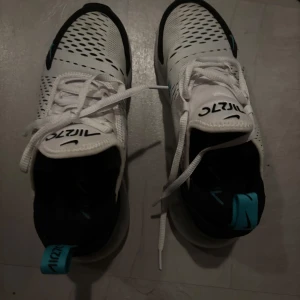 Nike 270 - Snygga vita sneakers från Nike med svarta och turkosa detaljer. Skorna har en modern design med perforerade mönster för ventilation och klassisk snörning. Perfekta för både träning och vardag.