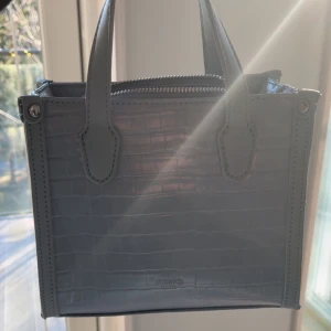 Blå handväska från Misako - Snygg blå handväska från Misako med krokodilmönster och dragkedja upptill. Perfekt för att ge din outfit en stilren touch. Väskan har två handtag och en rymlig insida för dina nödvändigheter, använd 1 gång. Pris kan diskuteras vid snabbt köp! 💗
