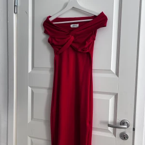 Röd klänning från Chiquelle - Snygg röd klänning från Chiquelle med en elegant knutdetalj framtill. Klänningen har en offshoulder-design som ger en stilren look. Perfekt för speciella tillfällen.