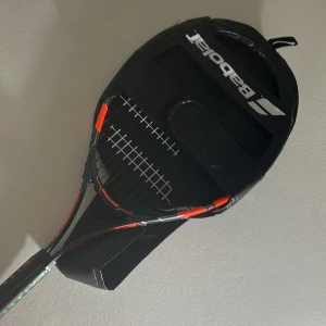 Svart och orange tennisracket från Babolat - Säljer ett stilrent svart och orange tennisracket från Babolat. Racketen har en svart ram med orange detaljer och kommer med ett matchande fodral med Babolat-logga. Perfekt för både nybörjare och erfarna spelare som vill ha kvalitet och stil på banan. Den är väldigt bra och ny. Har använt den max 4 gånger 