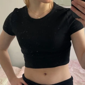 Svart croppad topp från Zara - Säljer en svart croppad topp från Zara i mjuk bomullsmix. Toppen har korta ärmar och en rund halsringning. Perfekt för en stilren look. 🌟