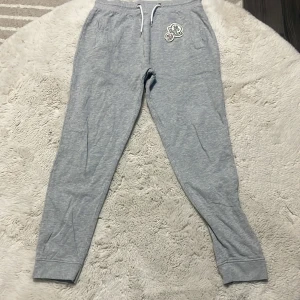 Grå mjukisbyxor från Moncler  - Snygga grå mjukisbyxor från Moncler med vit snörning i midjan och broderad Moncler-logga på ena benet. De är äkta