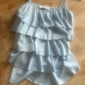 Ljusblå volangtop från By Swan - Supersöt ljusblå linnetopp från By Swan med flera lager volanger och smala axelband. Tunn och lätt i materialet. Köpt för nypris vilket är 299kr.