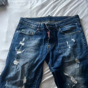 Blå shorts/ jeans för sommaren  från Dsquared2 - Säljer ett par blå jeans från Dsquared2 med slitna detaljer och trasiga partier framtill. Jeansen har klassisk femficksmodell, normal passform och tydliga slitningar för en trendig look. Perfekta för dig som gillar streetstyle.