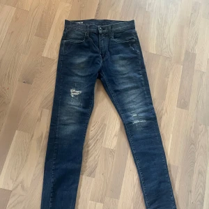 Jeans med slitningar från g star - Jeansen är helt nya‼️Säljer ett par mörkblå jeans från gstar med slitningar på låret och knät. Jeansen har fem fickor, klassisk passform och tydliga tvättade detaljer. Märkespatch bak i midjan och diskret logga på bakfickan. 