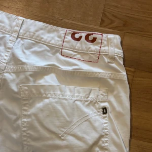Vita jeans från dondup  - Säljer ett par vita skinny jeans från George. Byxorna har klassisk femficksdesign, knapp- och dragkedjegylf samt dekorativ röd söm och detalj på bakfickan. Perfekta för dig som gillar en smal passform och stilren look.