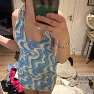 Blåvit mönstrad halterneckklänning från Gina Tricot - Supersnygg kort klänning från Gina Tricot med blått och vitt vågmönster. Halterneck med knyt i nacken och öppen rygg. Perfekt för sommarens alla tillfällen. Figurnära passform och mjukt material.