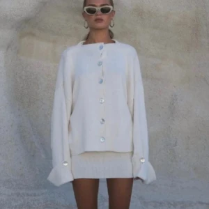 Krämvit kofta med pärlemorknappar - Säljer en oversized krämvit kofta med stora pärlemorknappar framtill. Koftan har långa ärmar och är tillverkad i ett mjukt, stickat material. Perfekt för lager-på-lager och enkel att styla till olika outfits.