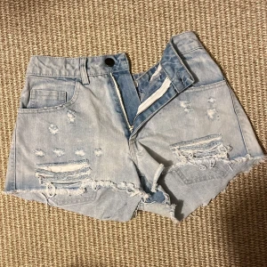 Ljusblå slitna jeansshorts - Säljer ett par ljusblå jeansshorts med hög midja och råa, fransiga kanter. Shortsen har slitningar och hål framtill, klassiska fickor både fram och bak samt knapp och dragkedja. Perfekta för sommaren! skriv privat för fler frågor eller bilder, kan även gå ner i pris💞jag har över sytt in dom som ni kan se på bild 2 men som sagt skriv för fler bilder.
