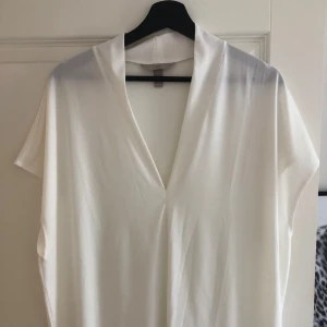 Vit v-ringad topp från H&M - Säljer en vit v-ringad topp från H&M i storlek XL. Toppen har korta ärmar och är tillverkad i ett mjukt, lätt material som faller snyggt. Perfekt för en stilren och enkel look.