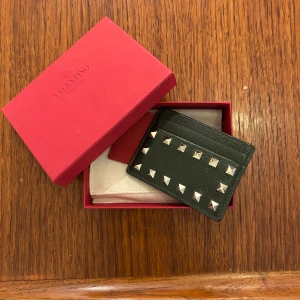 Valentino plånbok / korthållare med nitar  - Säljer en olivgrön korthållare från Valentino med  nitar runtom. Korthållaren är i skinn och har flera fack för kort. Mycket bra skick och enbart använd ett fåtal gånger.  Kommer i originalask och med dustbag och kvitto! Original pris 2300kr. (Pris kan diskuteras)