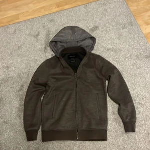 Brun hoodiejacka från Massimo Dutti - Snygg brun hoodiejacka från Massimo Dutti med dragkedja framtill och två fickor. Jackan har huva med dragsko och ribbade muddar vid ärmslut och nederkant. Tillverkad i ullblandning för extra komfort. Går ej att få tag på längre. Nypris 1699 Mitt pris: 999