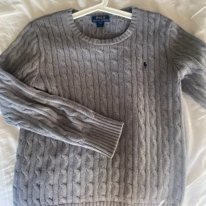 Grå kabelstickad tröja från Polo Ralph Lauren - Kabelstickad grå tröja från Polo Ralph Lauren. Perfekt för lager-på-lager-stil. Inga fläckar elr liknande, i stort sätt som ny. Storlek L barn, alltid öppen för frågor🤩