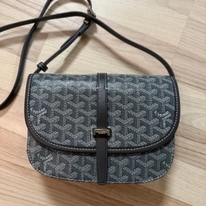 Svart axelväska  - Säljer en svart axelväska med klassiskt mönster och justerbar axelrem. Väskan har ett lock med metallspänne och insida i kontrasterande gul färg. Perfekt för dig som gillar stilrena accessoarer med lyxig känsla.