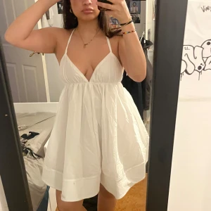 Vit kortklänning med korsade axelband - Superfin vit klänning med smala korsade axelband och öppen rygg. Klänningen har en lätt utsvängd kjol och knytning i ryggen för extra detalj. Perfekt för sommarens alla tillfällen! perfekt student klänning 