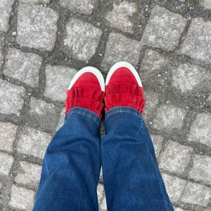 Röda sneakers med volangdetaljer - Säljer ett par röda sneakers med breda volangdetaljer framtill och vit sula. 