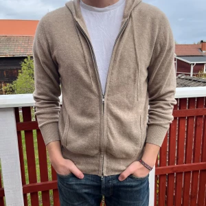 Beige hoodie i kashmir från Soft Goat - Beige fullzip kashmirhoodie från softgoat i storlek M. Extremt skön och är gjord av 100% kashmir. Använd sparsamt men har fått ett litet hål vid den vänstra armbågen (se sista bilden). Säljer eftersom jag inte har användning för den och för att jag inte orkar laga hålet, vilket säkert inte är speciellt svårt. Modellen är 180 och väger 77kg. Nypris 2995kr. 