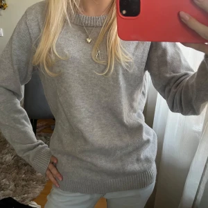Ljusgrå stickad tröja - Mysig ljusgrå stickad tröja med rund halsringning och ribbade muddar vid ärmslut och nederkant. Perfekt för lager-på-lager och enkel att matcha med olika outfits.