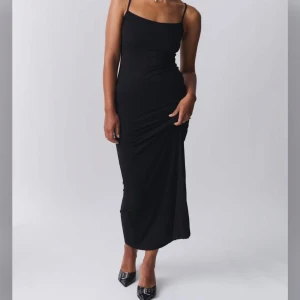 Svart långklänning med smala axelband - Säljer en stilren svart långklänning med smala axelband och figurnära passform. Klänningen har minimalistisk design och är perfekt för dig som gillar en enkel men elegant look.