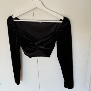 Svart croppad topp i sammet från Stradivarius - Säljer en svart croppad topp i sammet från Stradivarius. Toppen har lång ärm och en snygg twistad detalj framtill. Perfekt för att lyfta din outfit med en elegant touch.