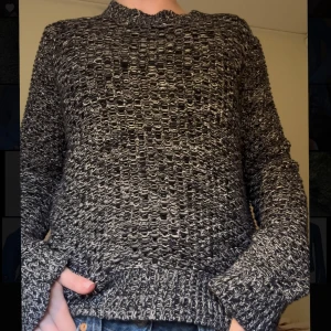 Svart och grå stickad tröja - Säljer en grovstickad svart och grå tröja med unikt mönster och rund hals. Tröjan har långa ärmar och ribbade muddar vid ärmslut och nederkant. Köpt secondhand på Stockholms stadsmission.