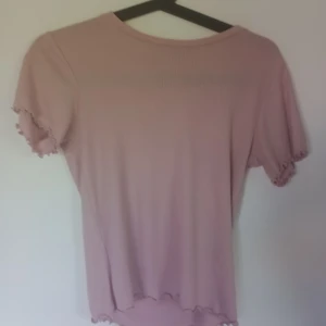 Rosa volang tshirt  - Rosa gullig t-shirt med volanger/vågor längst armarna, halsringningen och nedre delen. Tröjan är av ett lätt ribbat typ ( kolla sista bilden ) 